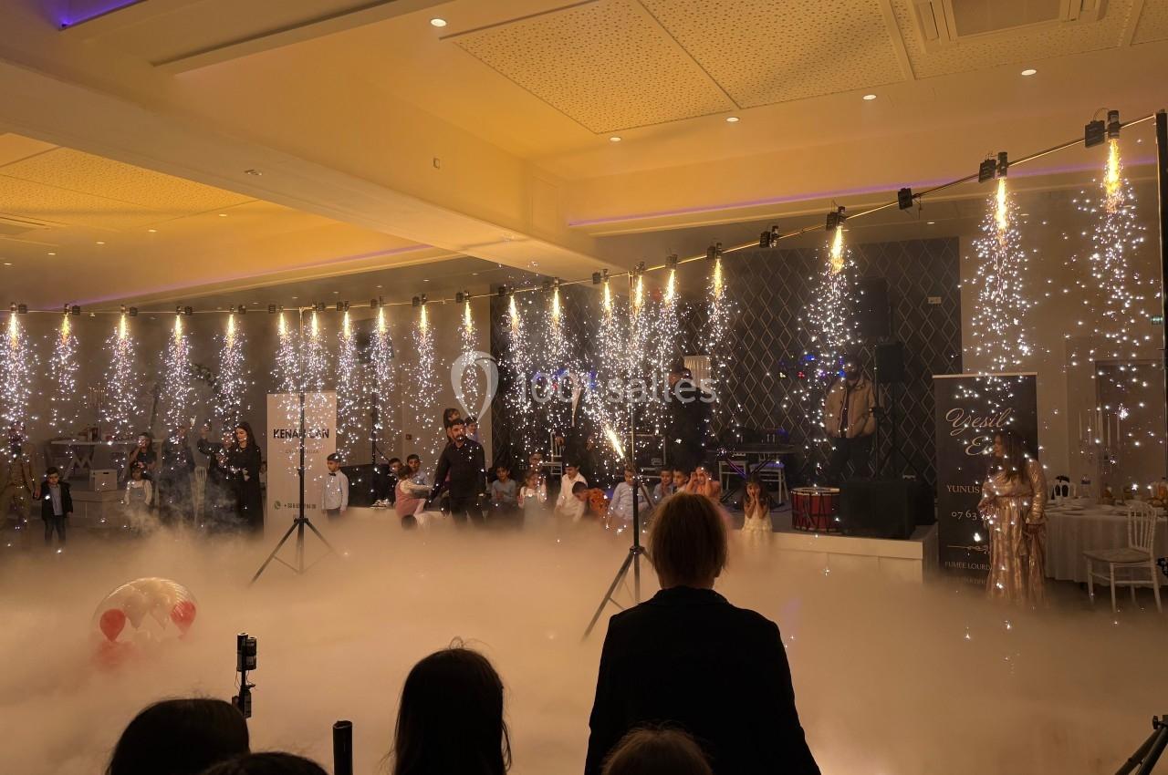 Salle de réception avec éclairage scintillant, fumée au sol et invités observant une scène festive.