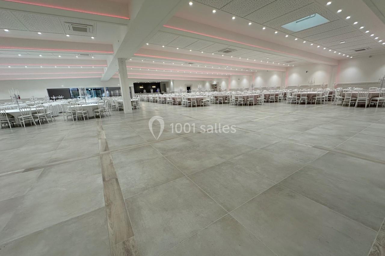 Salle de réception spacieuse avec tables et chaises blanches, éclairage au plafond et sol en carrelage clair.