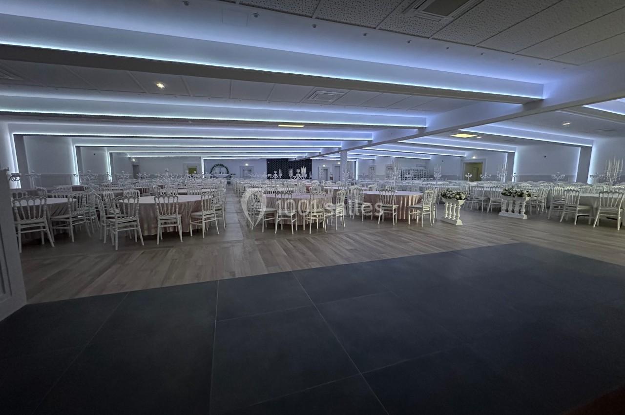 Salle de réception spacieuse avec des tables rondes dressées et des chaises blanches, éclairage moderne au plafond.