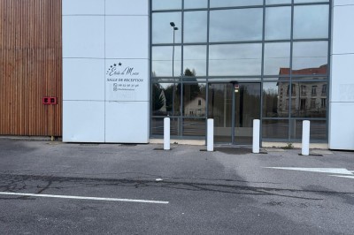 Façade d'un bâtiment moderne avec des murs en bois et en verre, entouré d'un grand parking vide.