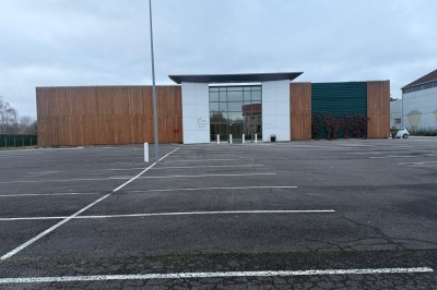 Façade d'un bâtiment moderne avec des murs en bois et en verre, entouré d'un grand parking vide.