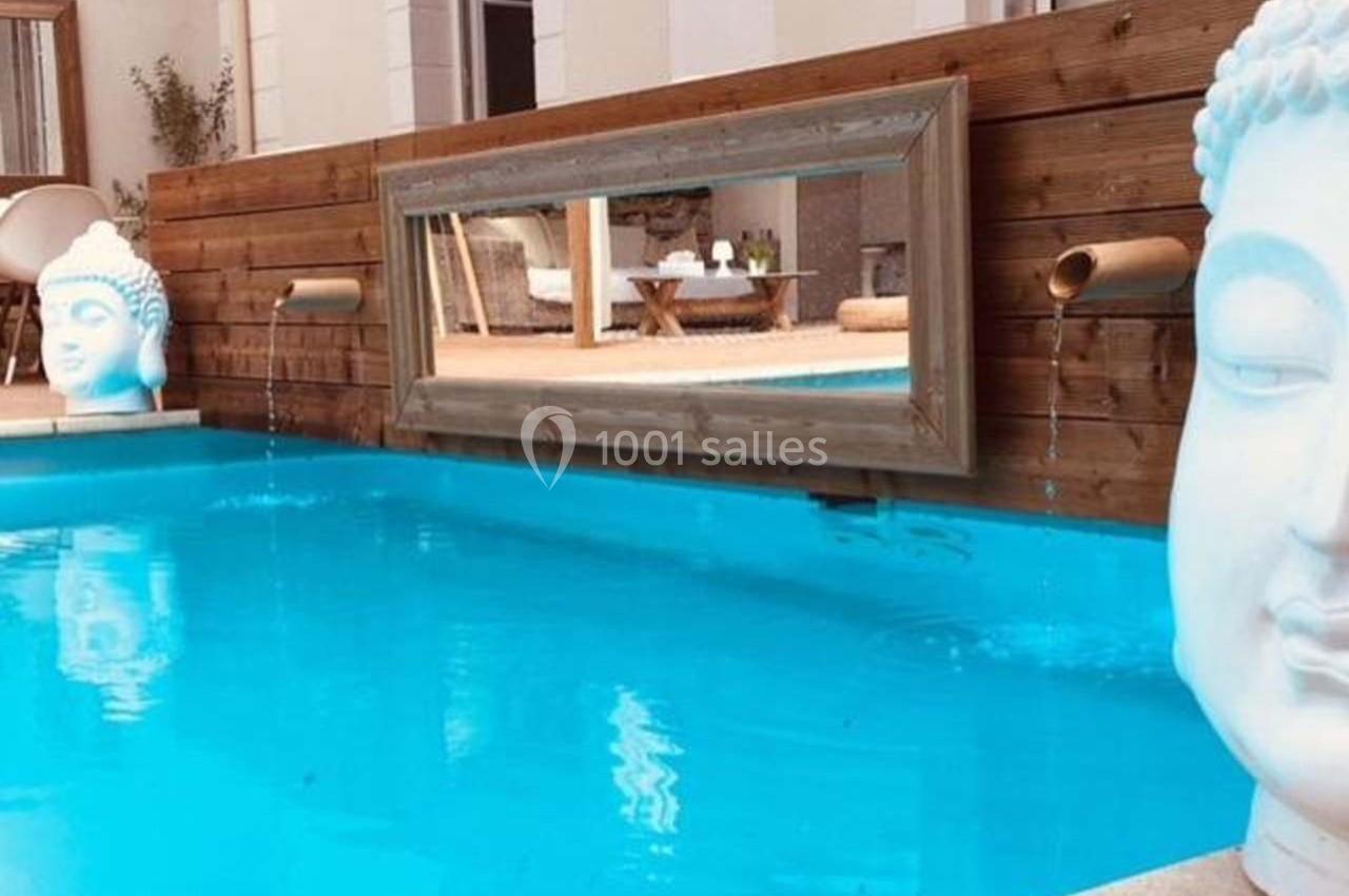 Piscine avec eau turquoise, ornée de statues de Bouddha et de fontaines en bambou sur un mur en bois.