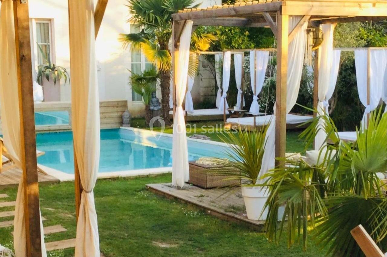 Piscine extérieure entourée de pergolas en bois avec rideaux blancs, transats et végétation tropicale.