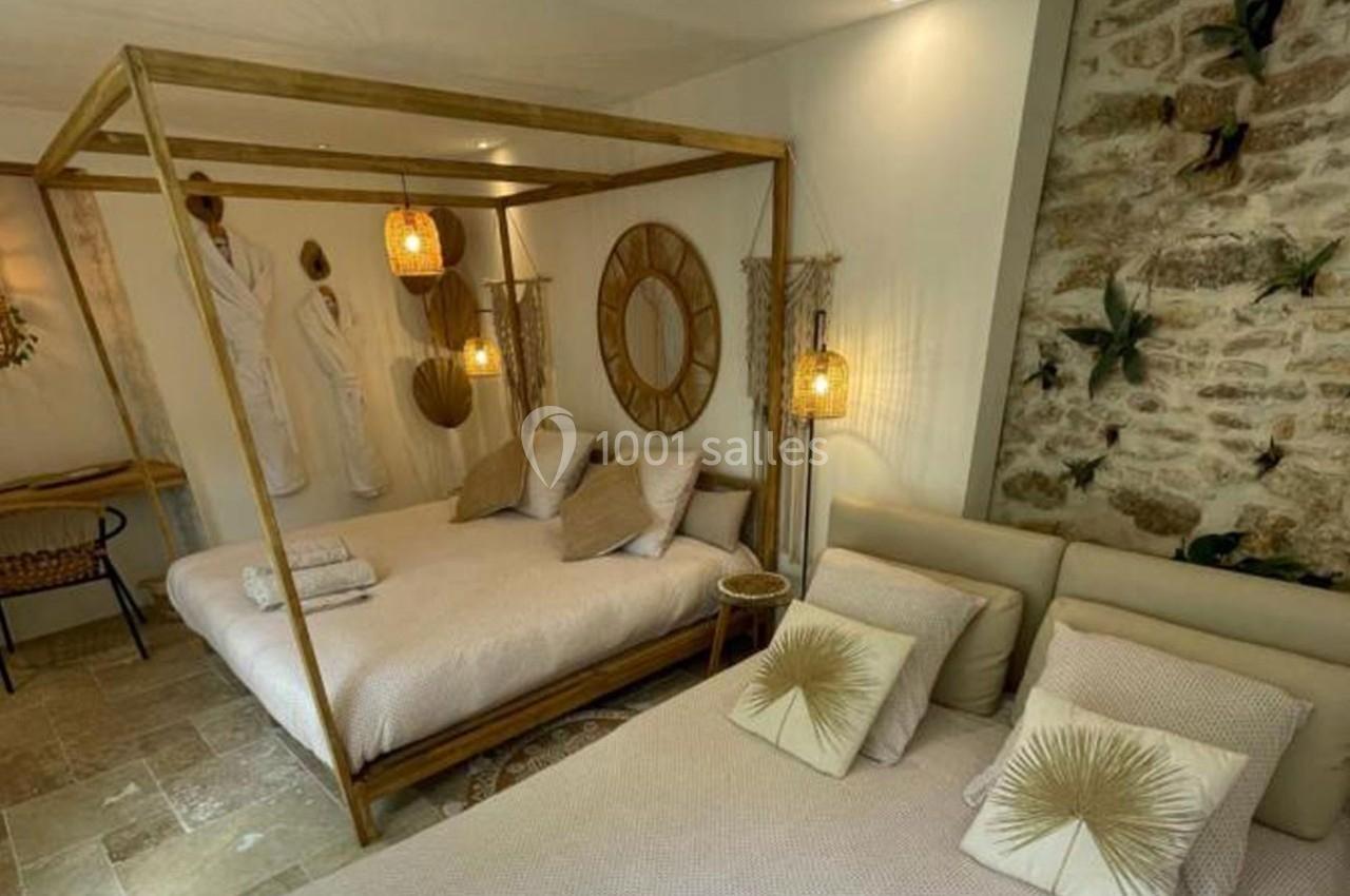 Chambre lumineuse avec lit à baldaquin en bois, décorée de tons naturels, murs en pierre et luminaires suspendus.