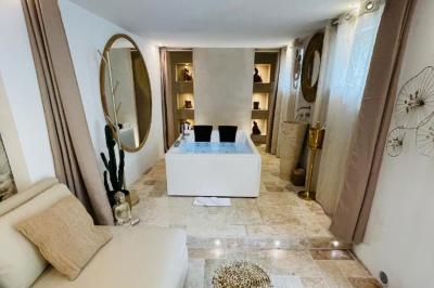 Chambre lumineuse avec jacuzzi intégré, lit double, murs en pierre blanche et décoration élégante.