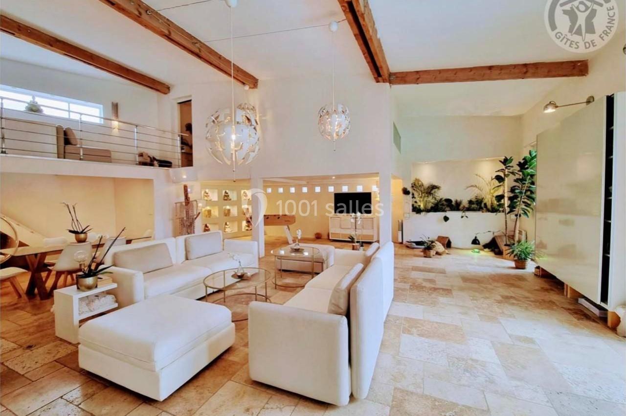 Salon spacieux et lumineux avec canapés blancs, poutres apparentes, plantes et décoration moderne.