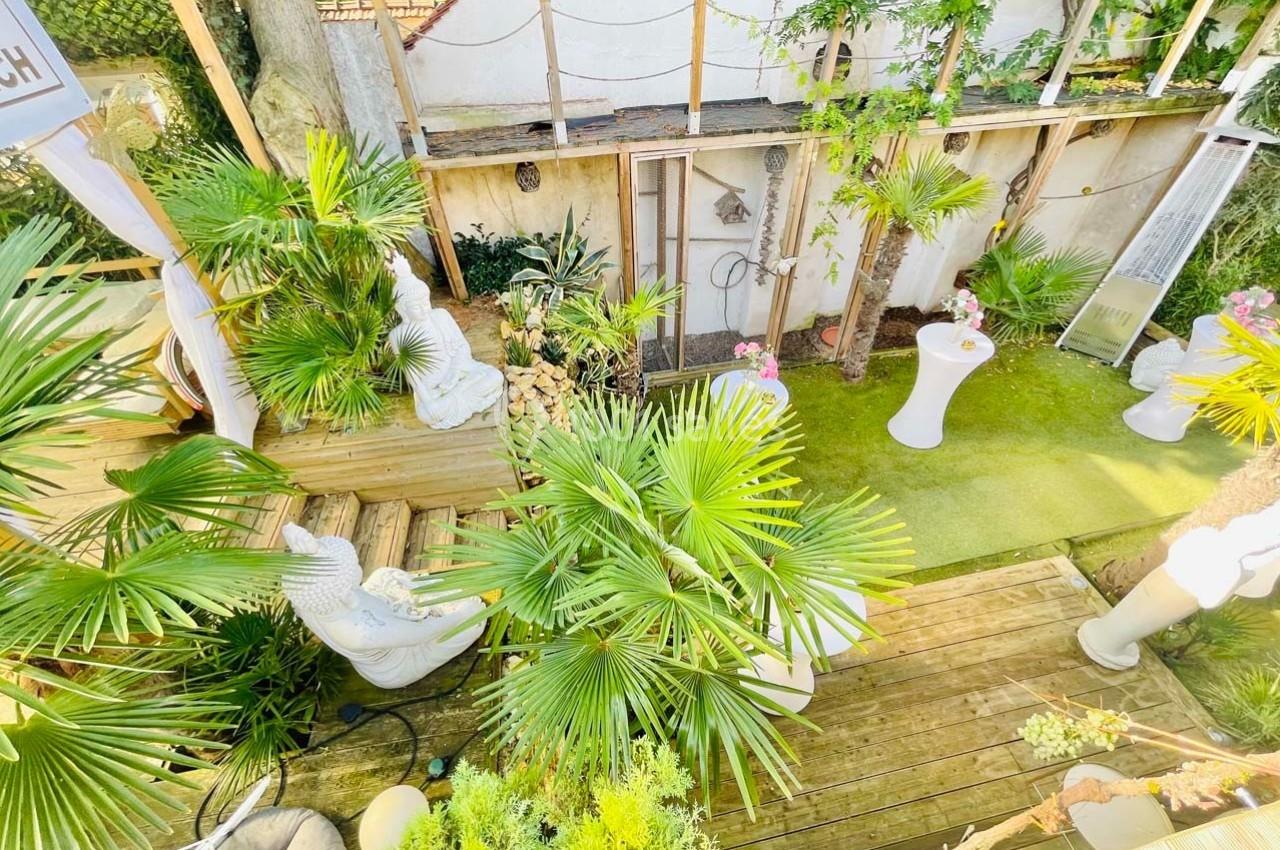 Vue d'un jardin aménagé avec des plantes tropicales, des statues décoratives et une terrasse en bois.