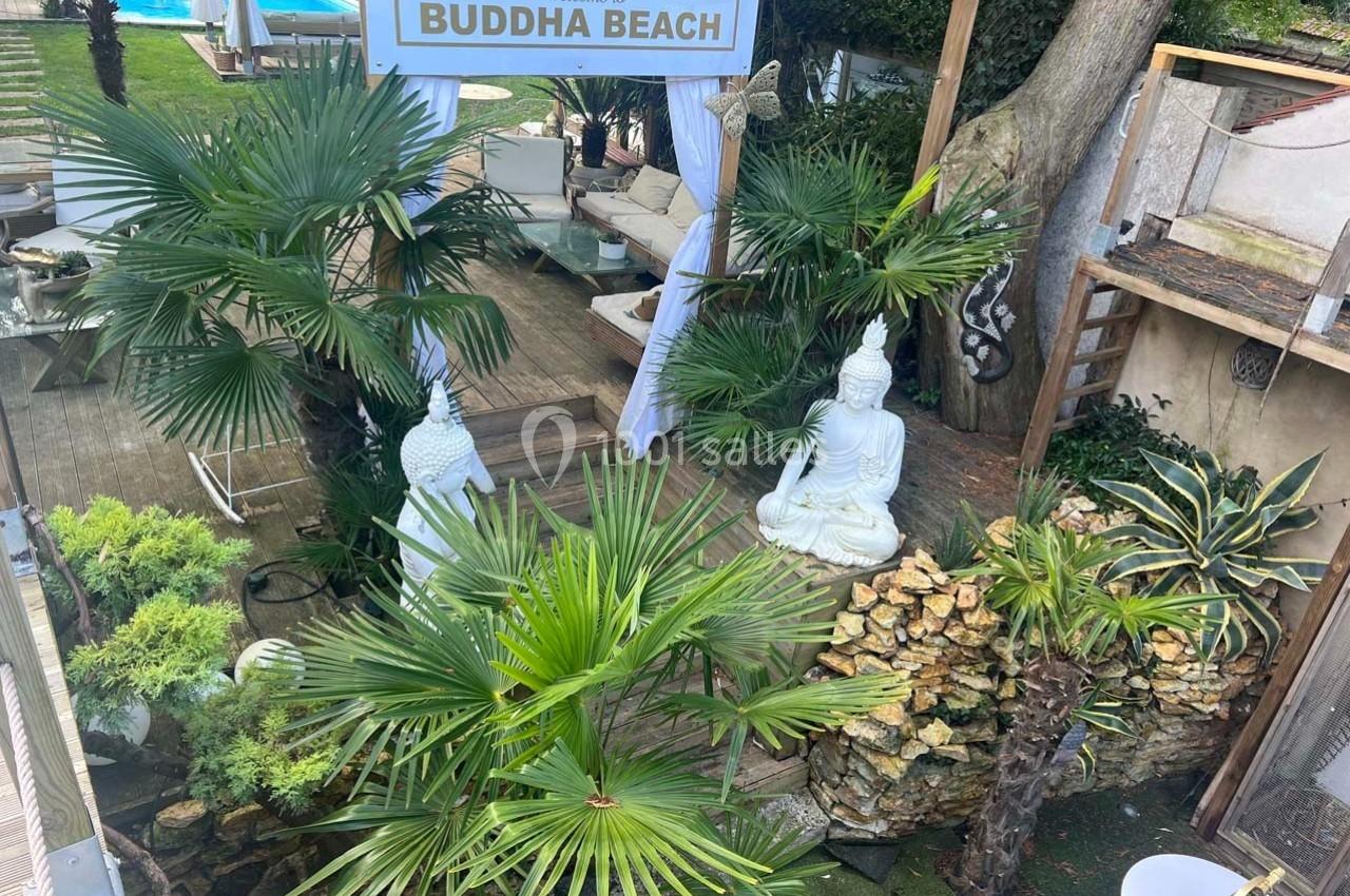 Espace extérieur avec statues de Bouddha, végétation tropicale et mobilier de jardin près d'une piscine.