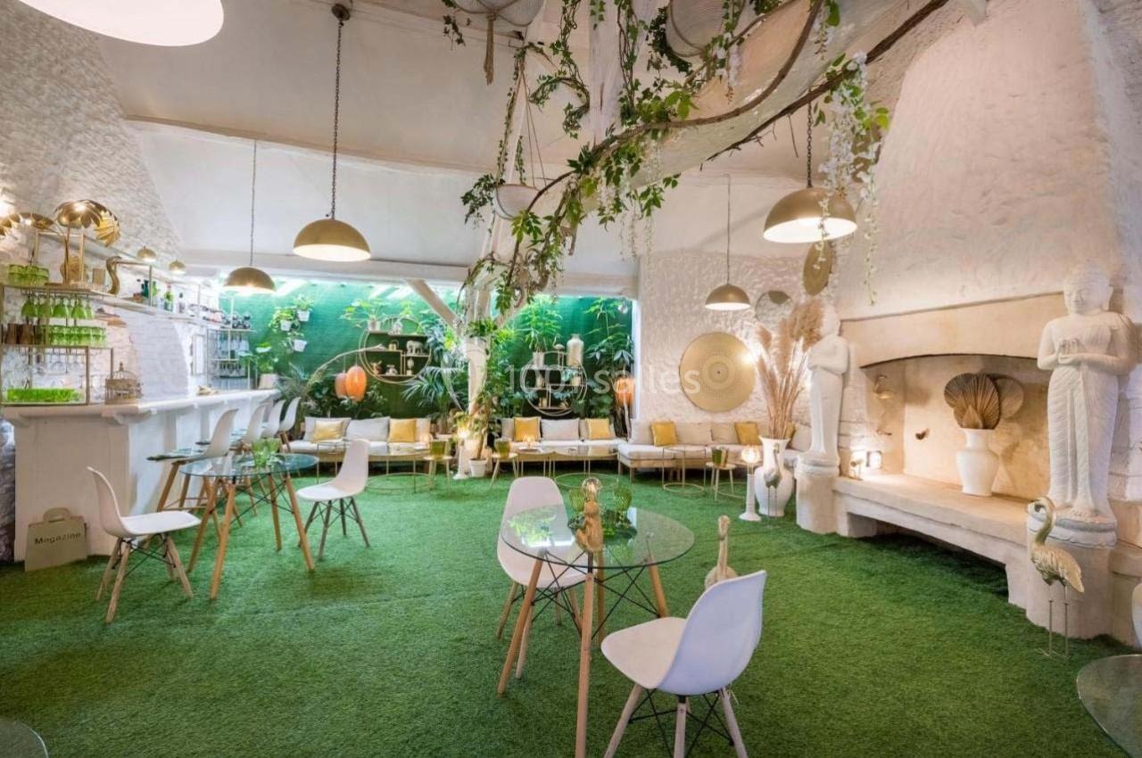 Salle lumineuse avec décoration végétale, mobilier moderne, sol en gazon artificiel et statues blanches.