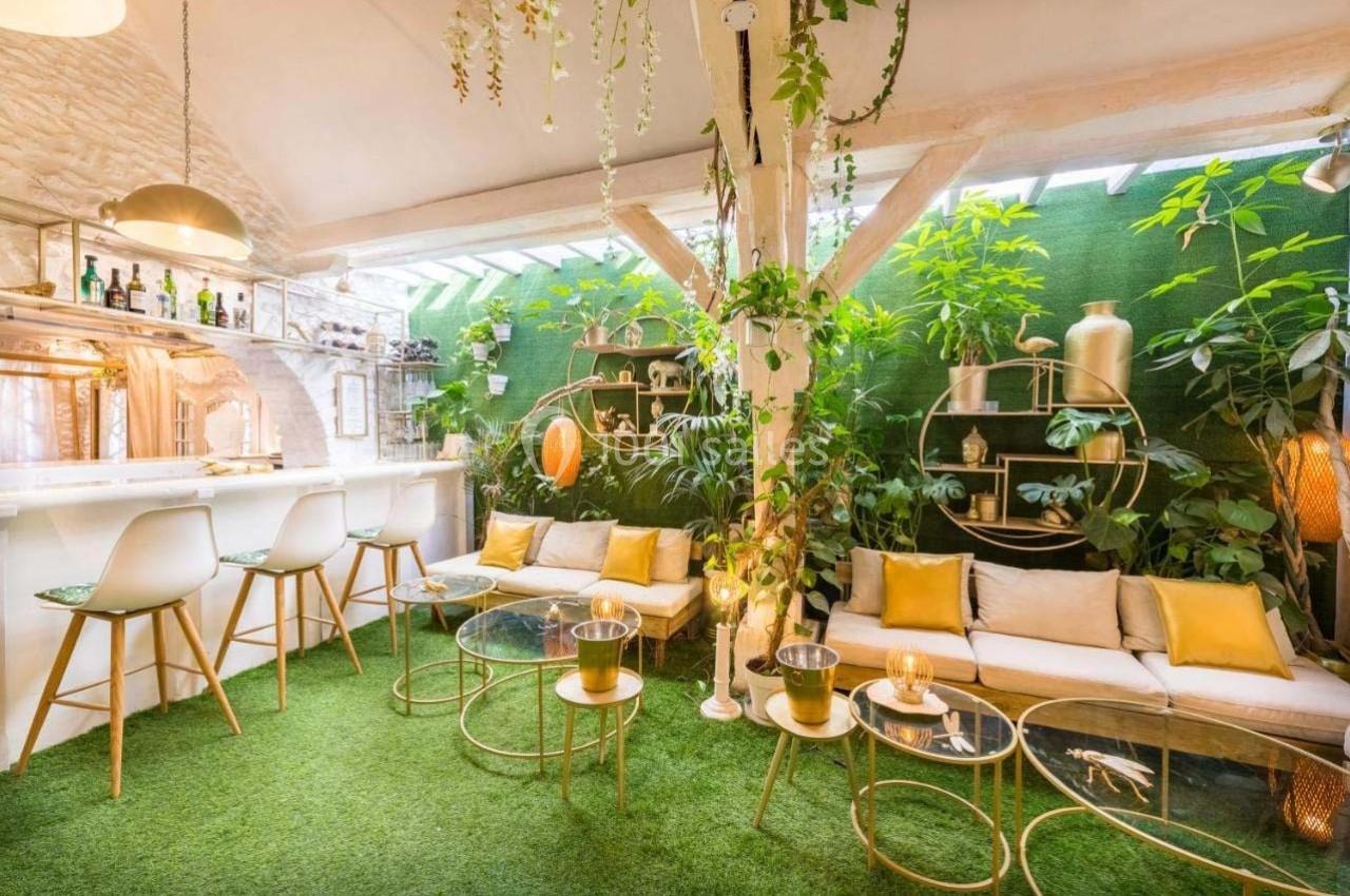 Espace intérieur lumineux avec bar, mobilier moderne, plantes vertes et sol recouvert de gazon artificiel.