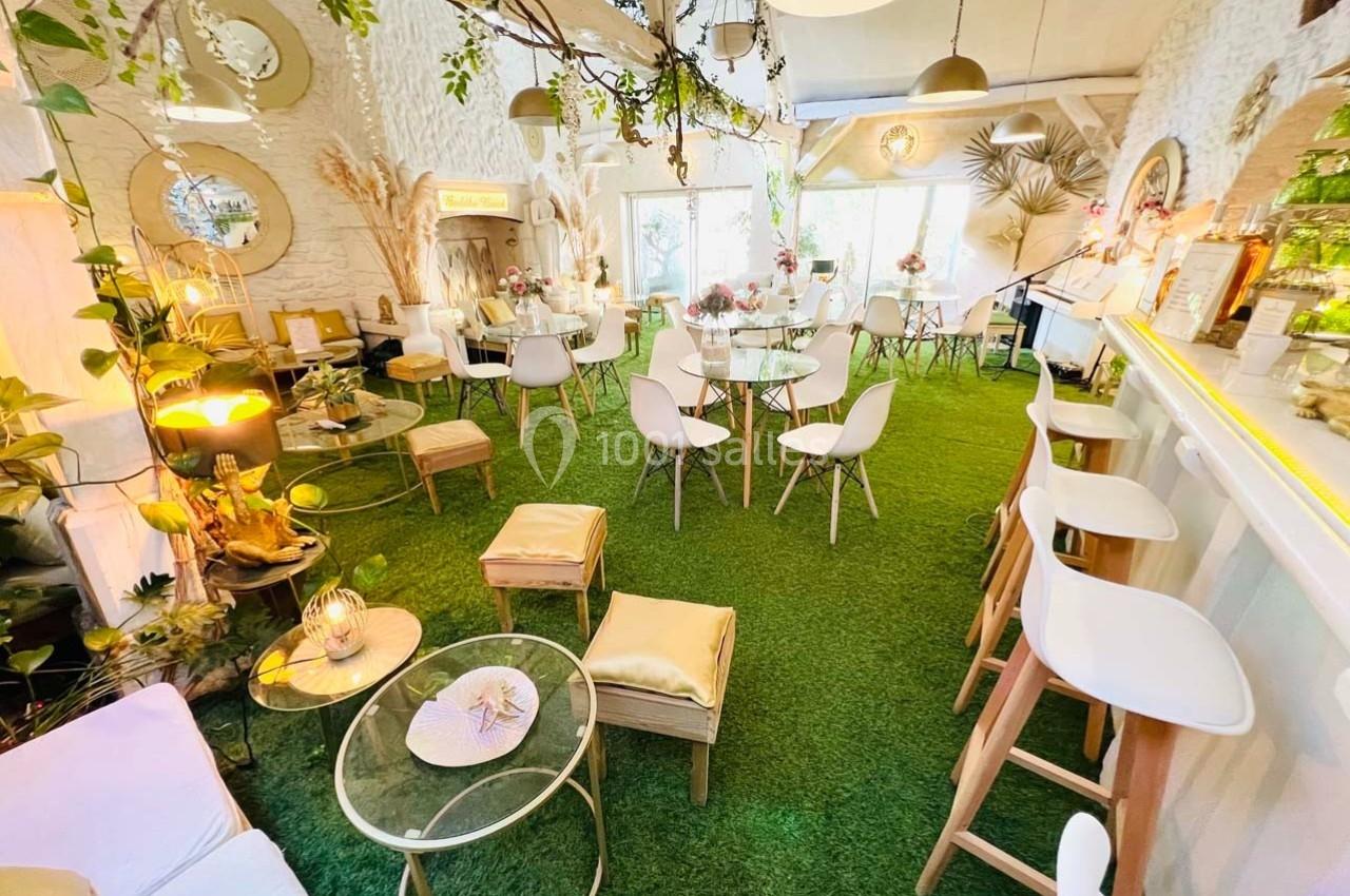 Salle lumineuse avec décoration végétale, mobilier moderne et sol recouvert de gazon artificiel.