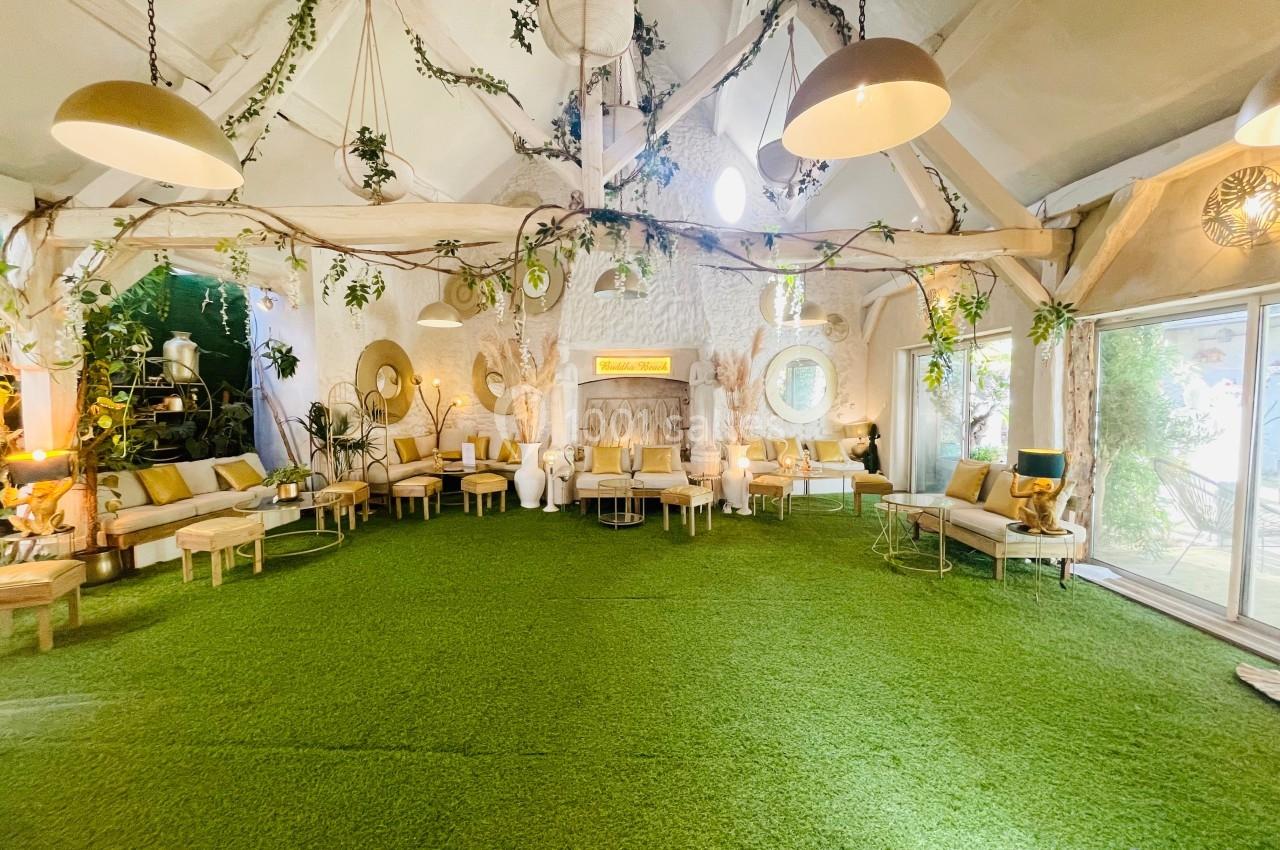 Salle lumineuse avec sol en gazon artificiel, mobilier clair, plantes suspendues et grandes baies vitrées.