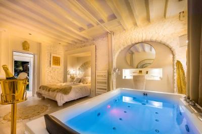 Chambre lumineuse avec jacuzzi intégré, lit double, murs en pierre blanche et décoration élégante.
