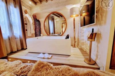 Chambre lumineuse avec jacuzzi intégré, lit double, murs en pierre blanche et décoration élégante.