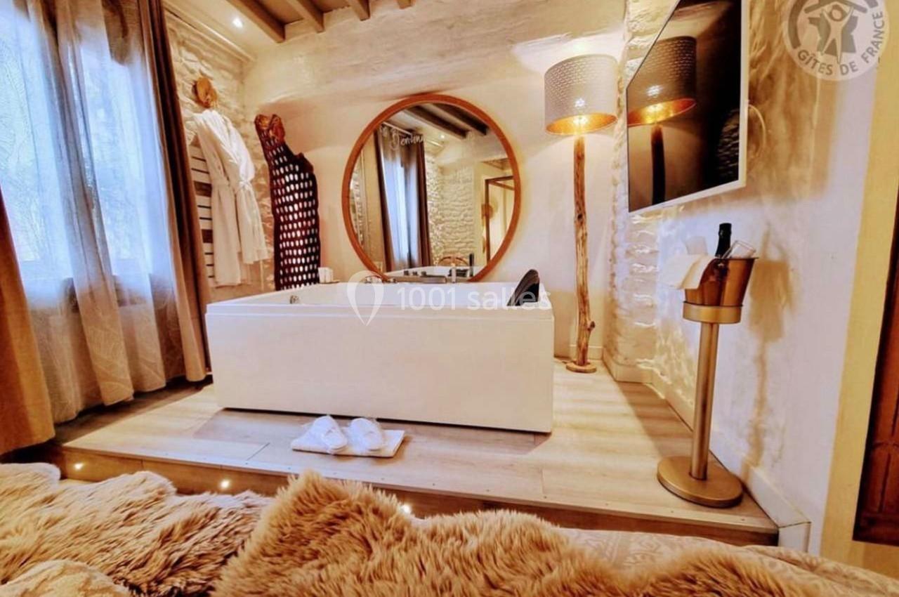 Salle de bain chaleureuse avec baignoire blanche, miroir rond, peignoirs accrochés et éclairage doux.