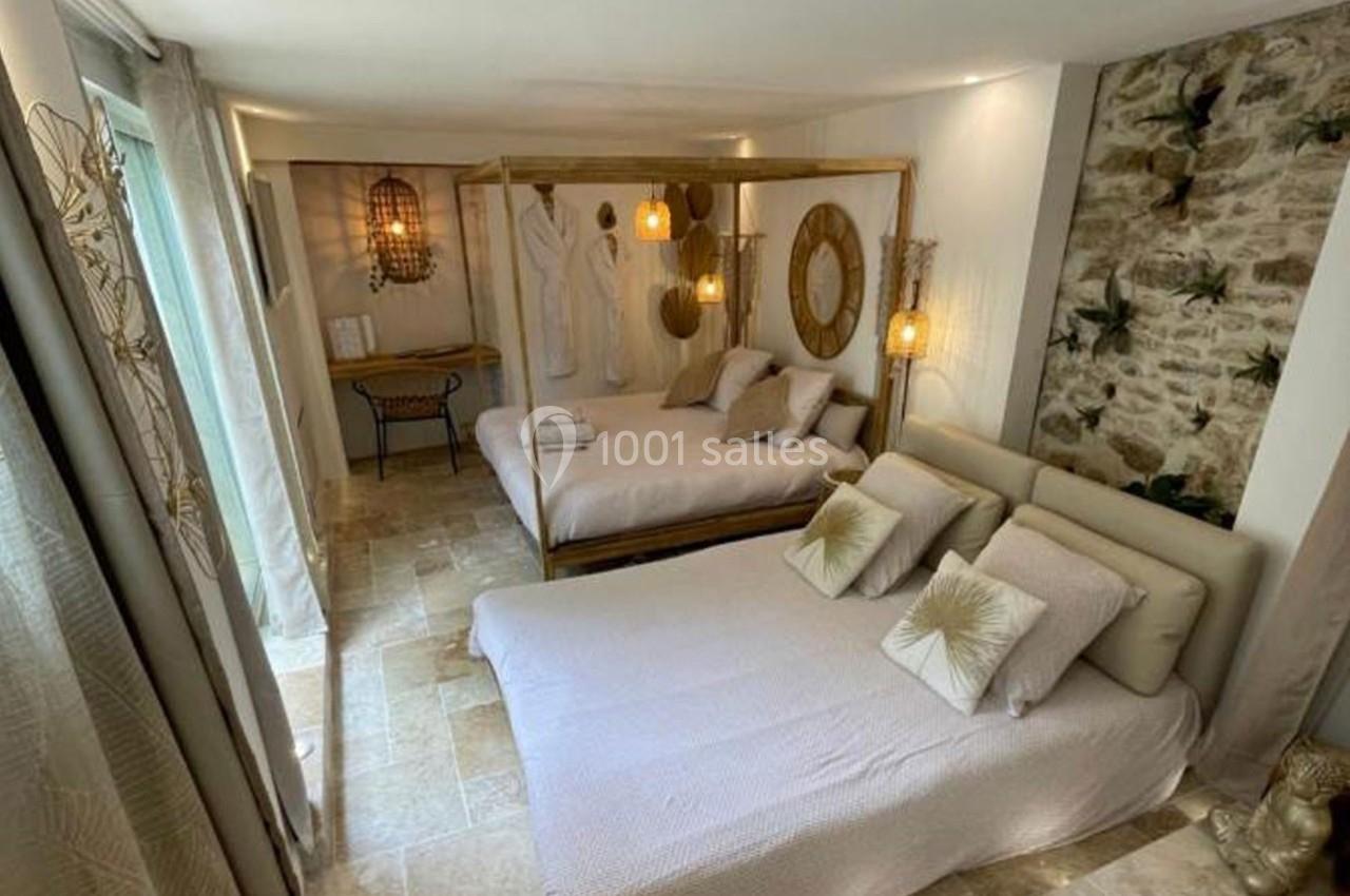 Chambre lumineuse avec deux lits doubles, décorée avec des tons naturels, des pierres apparentes et des luminaires suspendus.