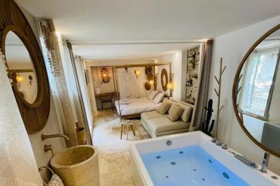 Chambre lumineuse avec jacuzzi intégré, lit double, murs en pierre blanche et décoration élégante.