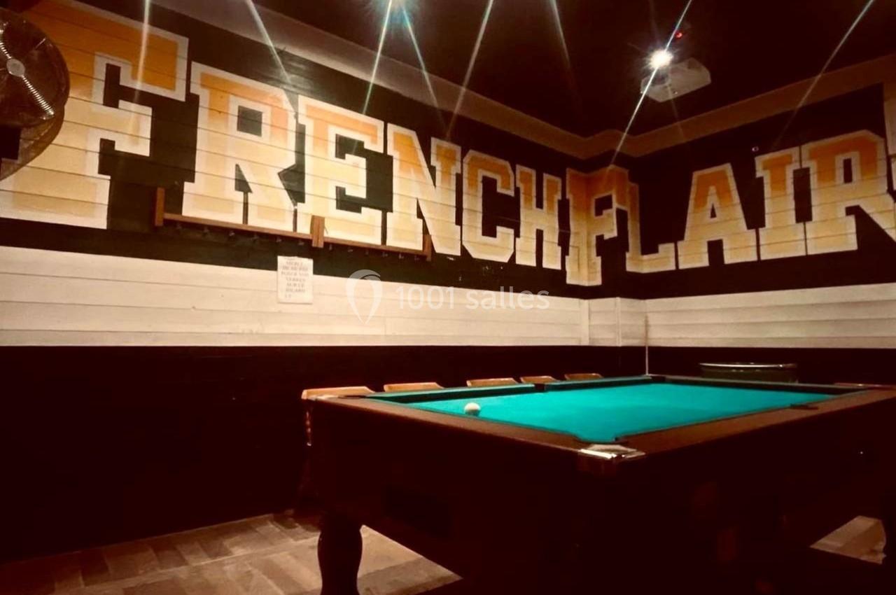 Table de billard dans une salle sombre avec des murs décorés du texte ’French Flair’ en grandes lettres.