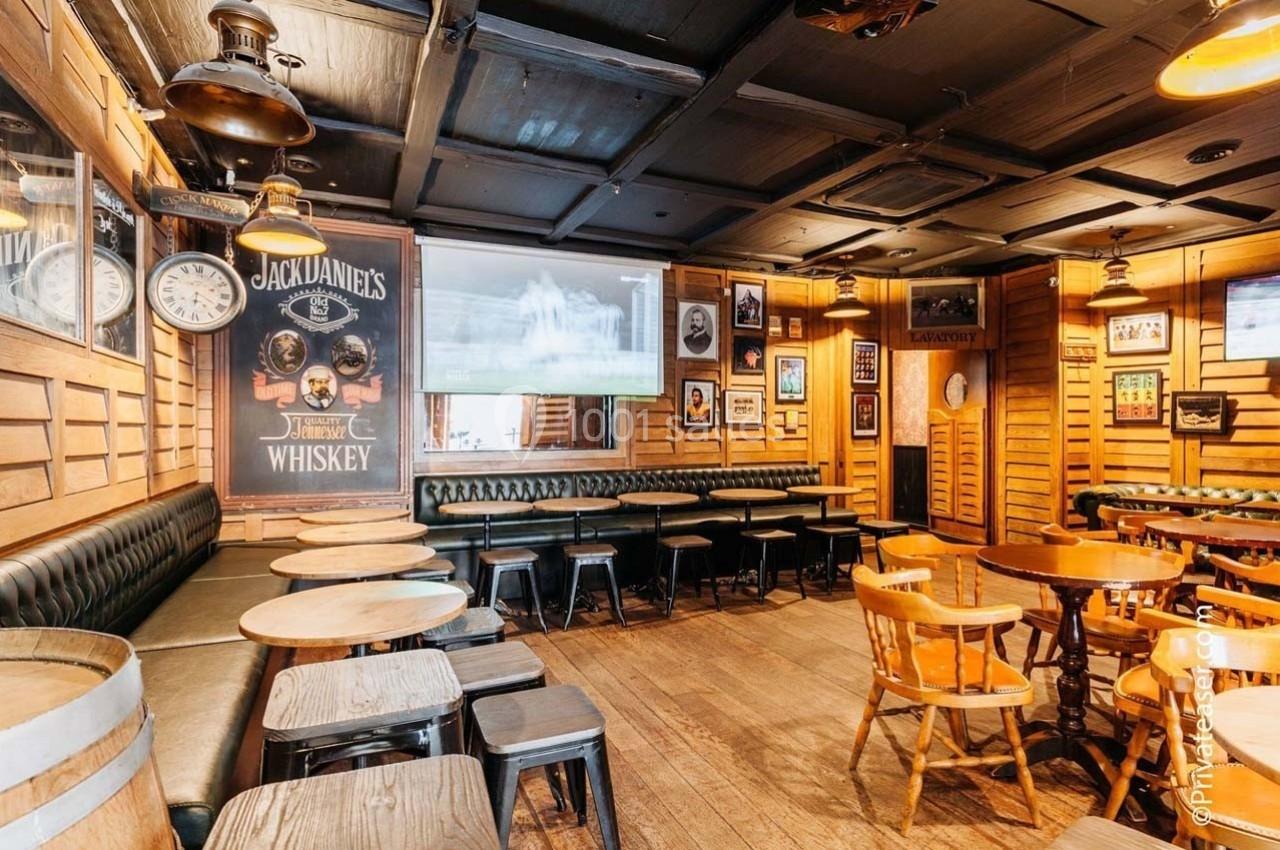 Salle de bar en bois avec tables rondes, chaises, banquettes noires et décorations murales variées.