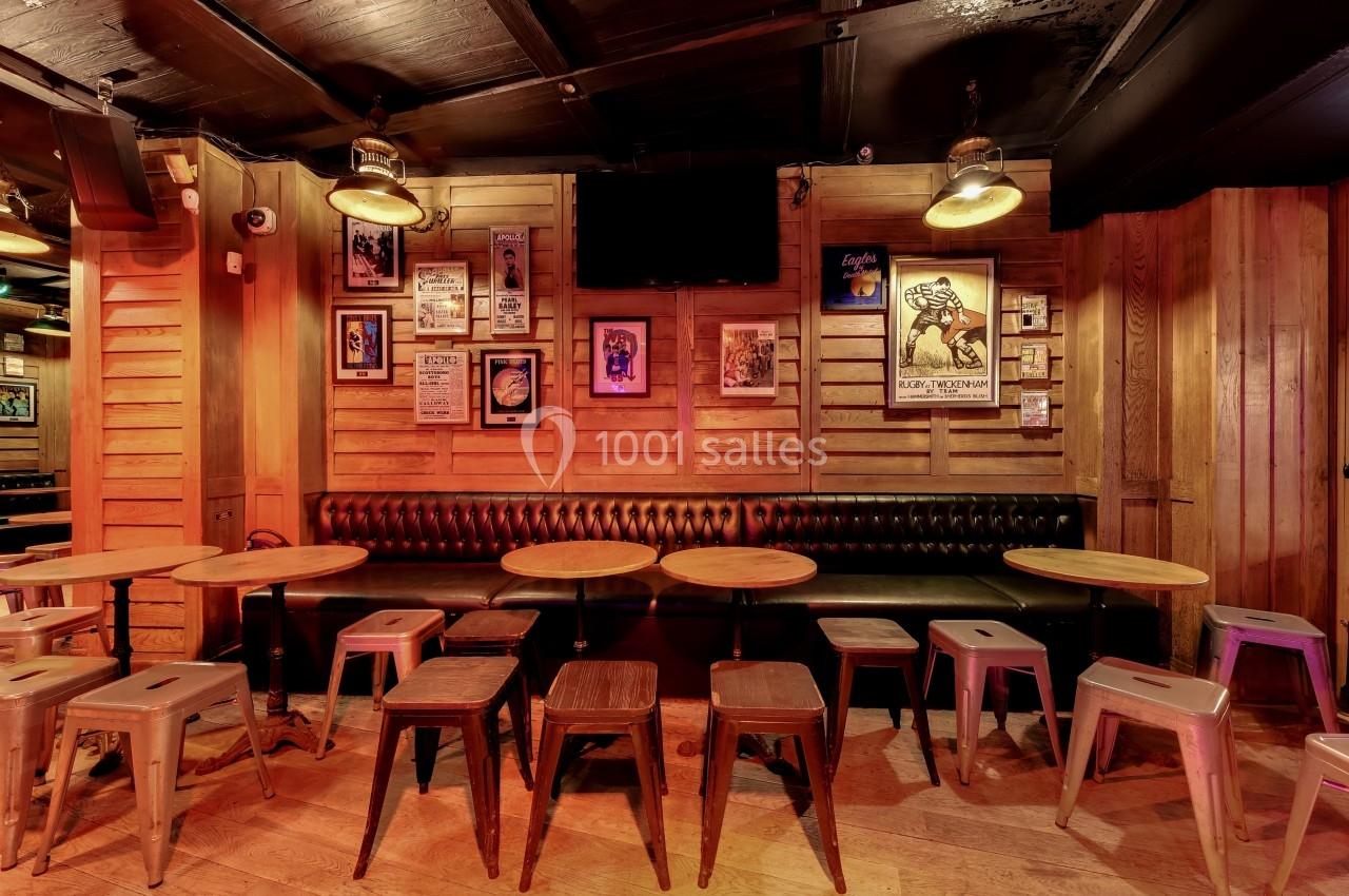 Banquettes en cuir noir, tables rondes en bois et tabourets dans un bar à l'ambiance chaleureuse avec murs décorés d…