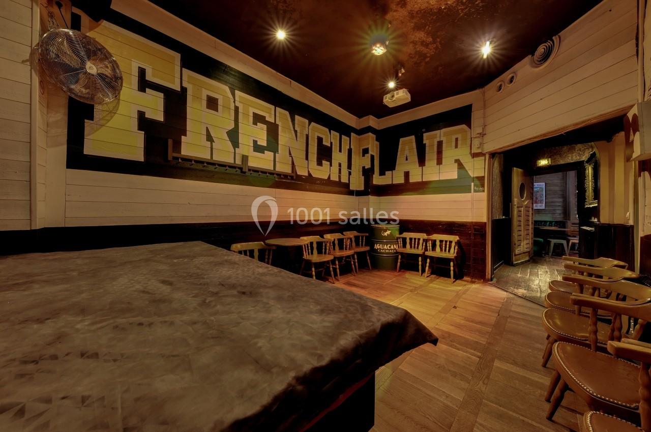 Salle de bar avec des murs en bois, des tables et chaises alignées, et une grande inscription ’French Flair’ sur le mur.