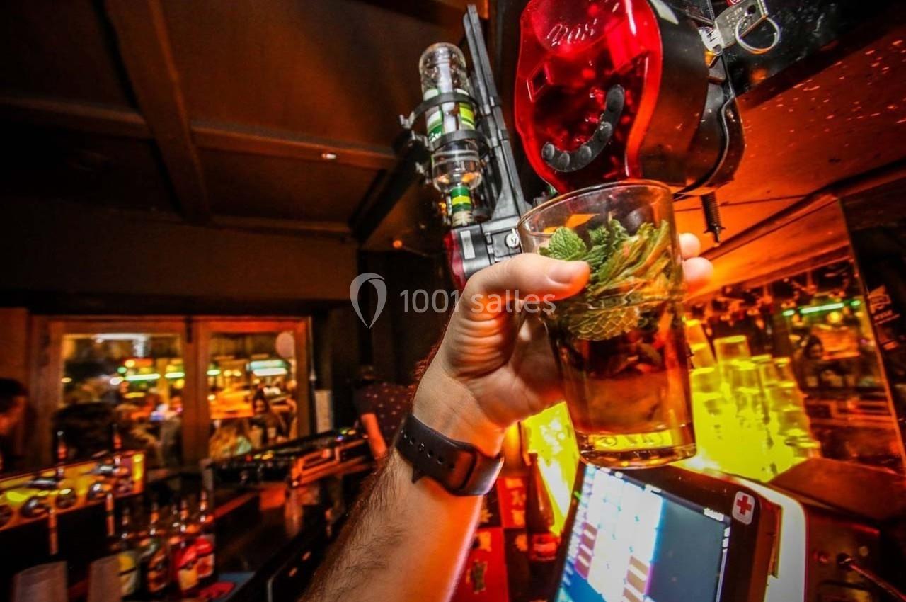 Un verre de cocktail garni de menthe est tenu devant un distributeur de boissons dans un bar éclairé.