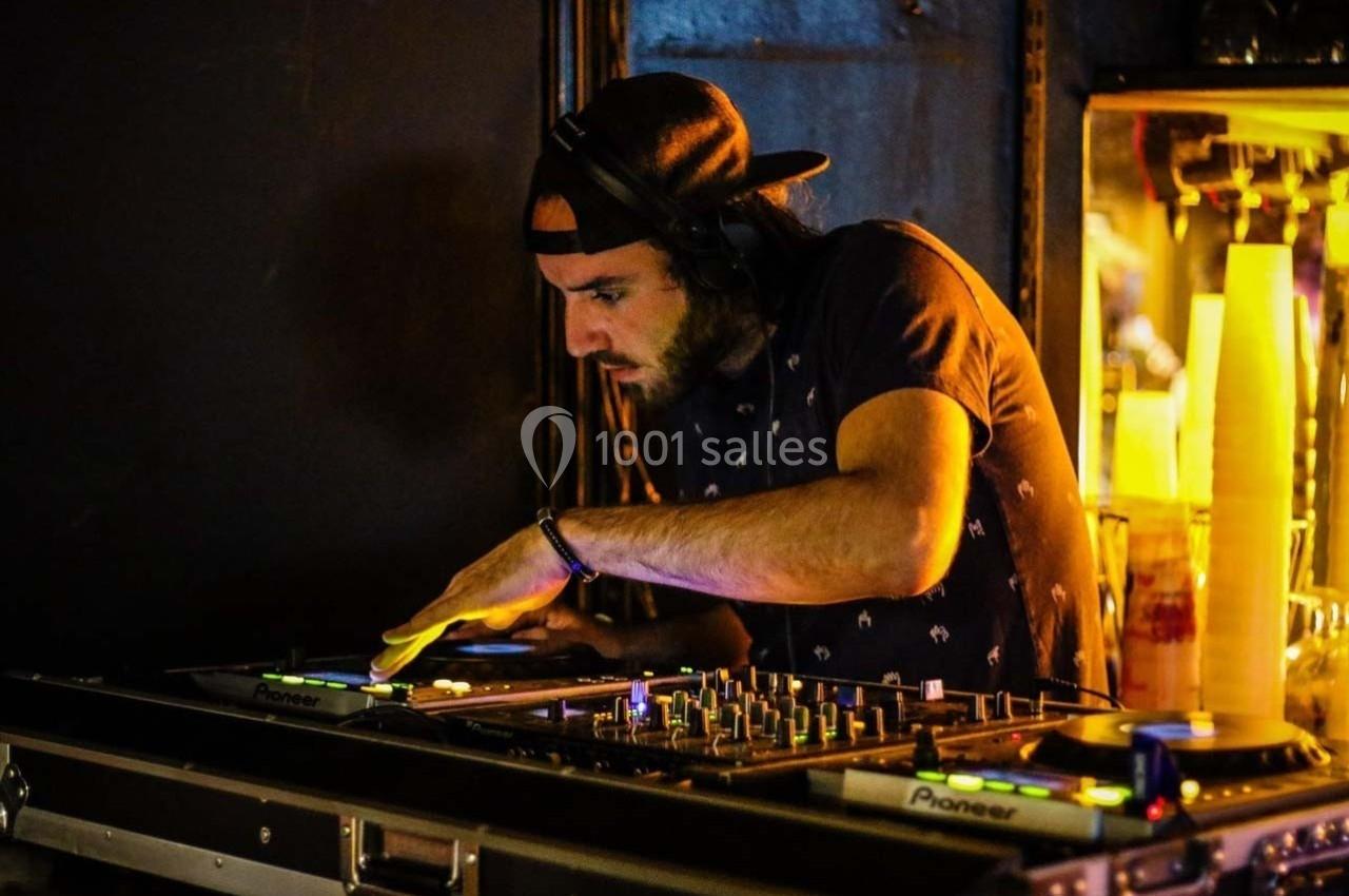 Un DJ mixe de la musique sur une table de mixage dans une ambiance sombre et lumineuse.