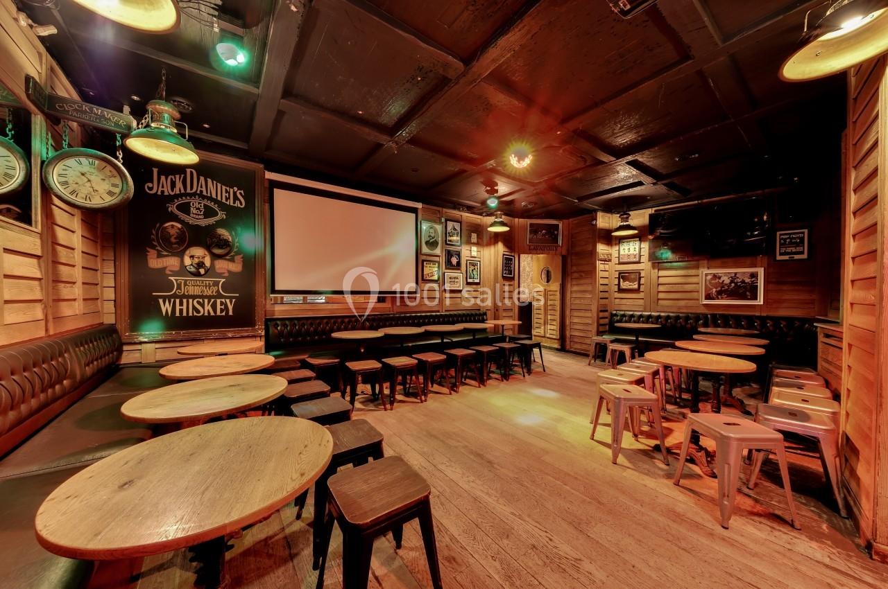 Salle de bar chaleureuse avec tables en bois, tabourets métalliques et décoration murale rétro sous un éclairage tamisé.