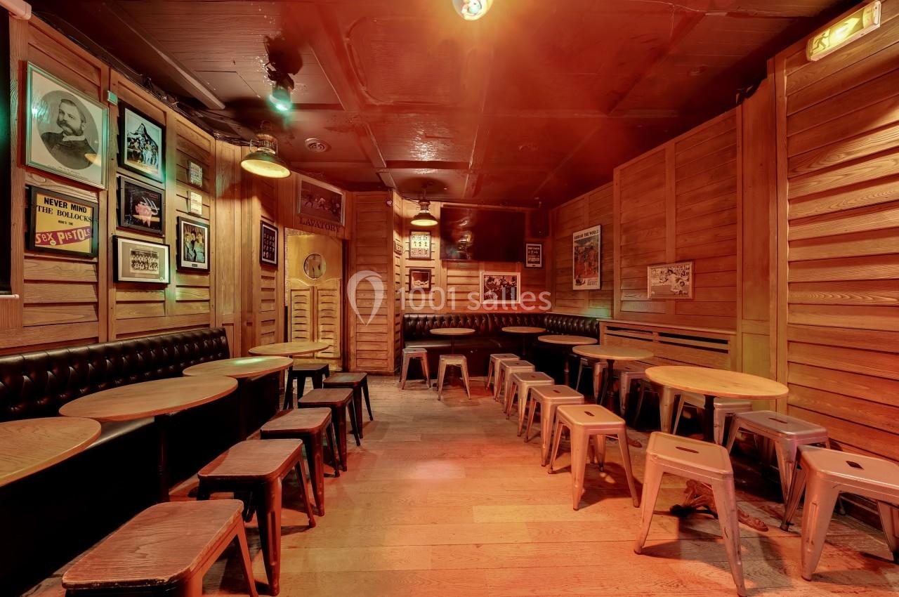 Salle en bois avec tables rondes, tabourets métalliques et murs décorés d'affiches rétro.