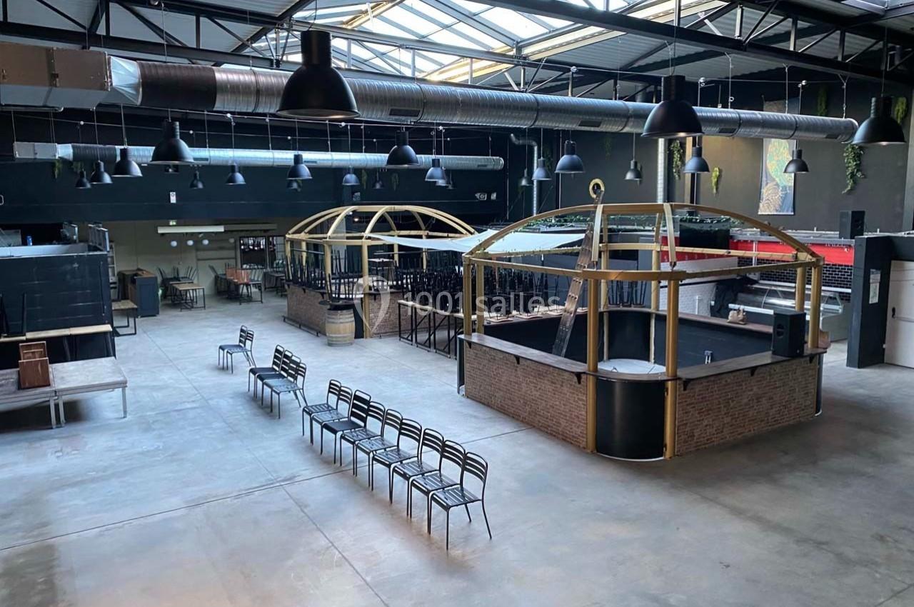 Intérieur d'un grand espace industriel avec un bar central en briques, des chaises alignées et un plafond métallique.