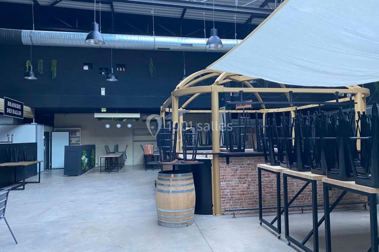 Salle de restaurant vide avec chaises empilées sur les tables, structure en bois et tonneau au premier plan.