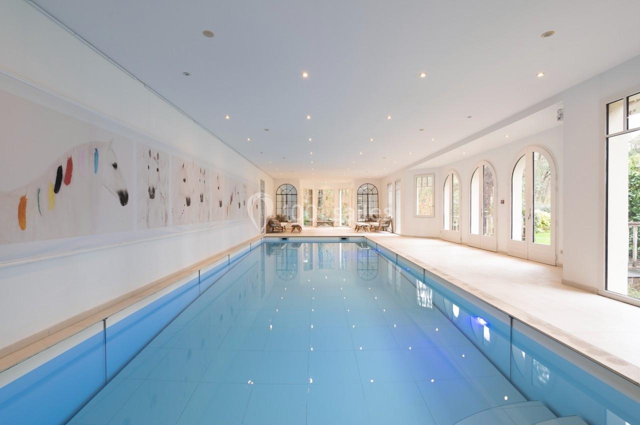 Piscine intérieure lumineuse avec carrelage bleu, grandes baies vitrées et décoration murale artistique.