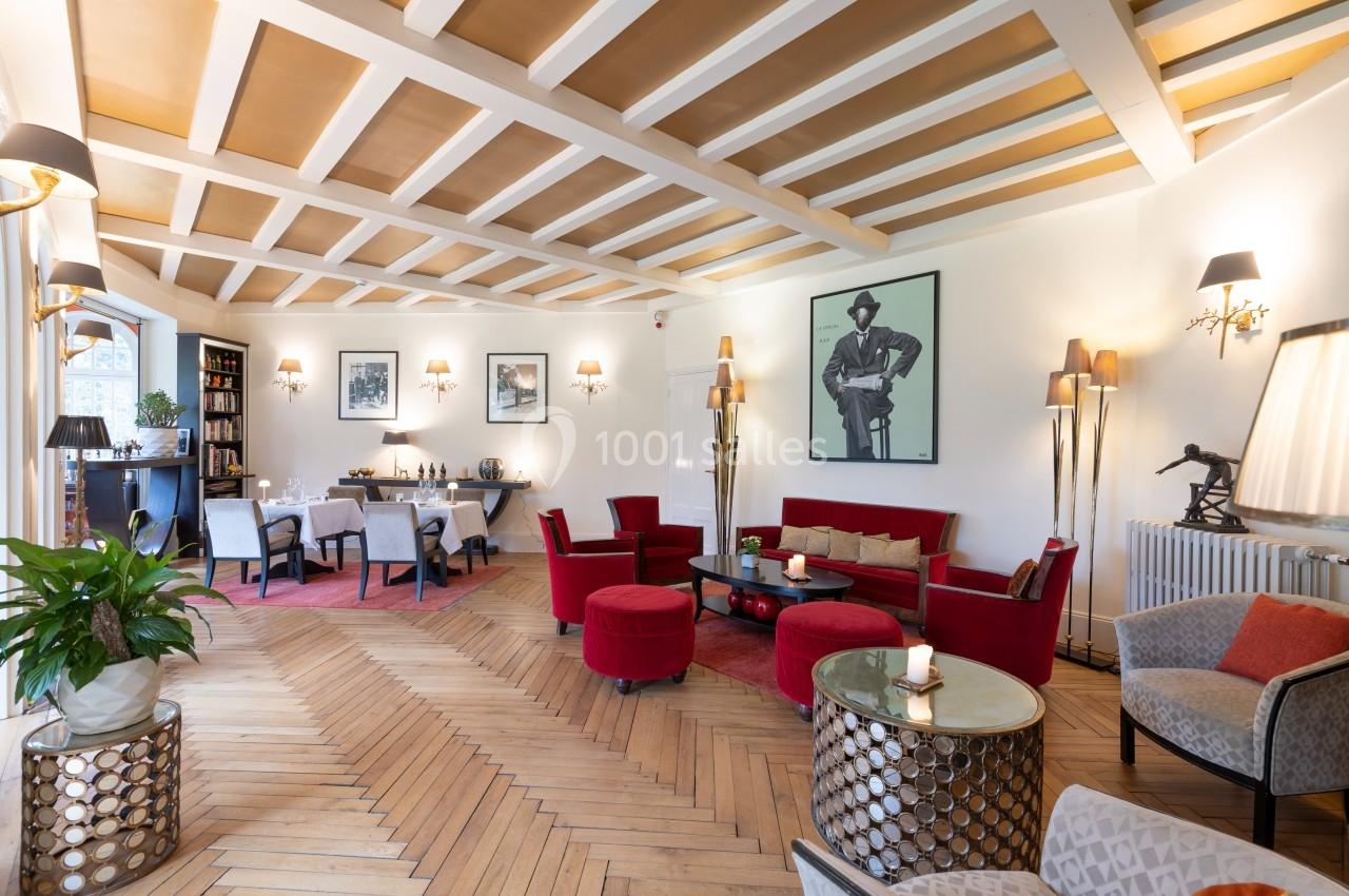 Salon élégant avec parquet en chevron, mobilier rouge et beige, œuvres d'art aux murs et lumière naturelle abondante.