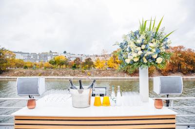 Bateau naviguant sur une rivière avec des passagers debout sur le pont supérieur près d'un quai en pierre.