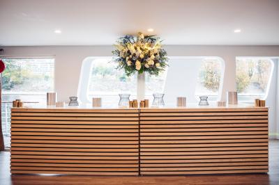 Bateau naviguant sur une rivière avec des passagers debout sur le pont supérieur près d'un quai en pierre.