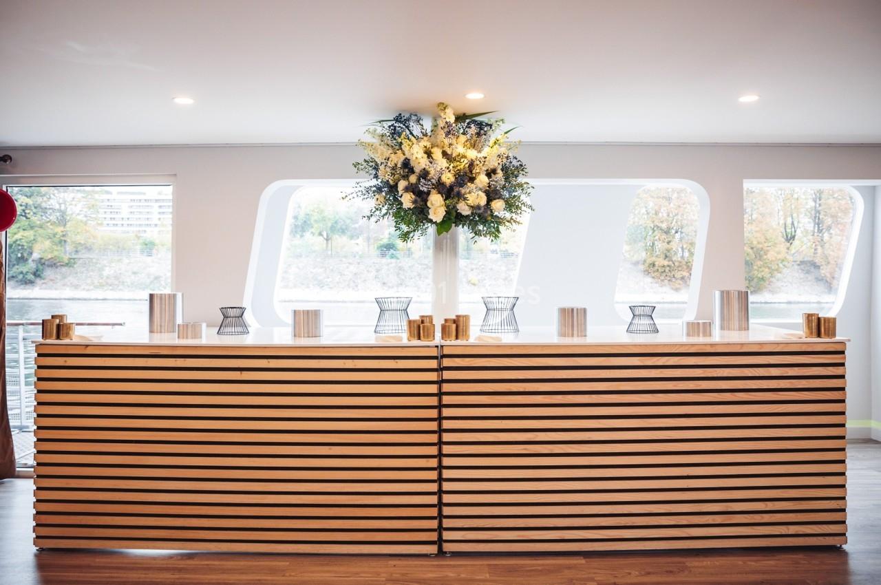 Comptoir en bois clair décoré d'un grand bouquet de fleurs blanches et jaunes, dans un espace lumineux avec vue extérieure.