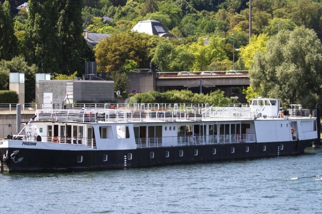 Bateau à quai sur une rivière, entouré de végétation et de bâtiments en arrière-plan.