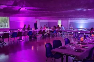 Salle de réception décorée avec des tables dressées, éclairage violet et quelques convives assis ou debout.