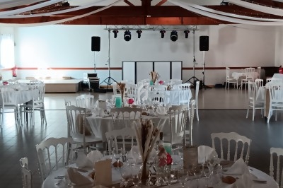 Salle de réception décorée avec des tables rondes dressées, des nappes blanches et des guirlandes suspendues.