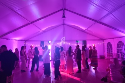 Personnes dansant sous une tente éclairée par des lumières colorées lors d'un événement festif en soirée.
