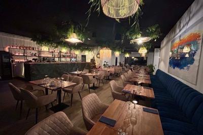 Terrasse d'un restaurant avec des tables dressées, située devant un immeuble moderne et un parking ensoleillé.