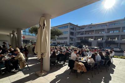 Terrasse d'un restaurant avec des tables dressées, située devant un immeuble moderne et un parking ensoleillé.