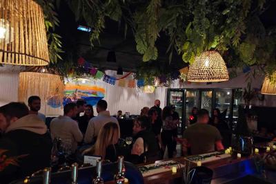 Terrasse d'un restaurant avec des tables dressées, située devant un immeuble moderne et un parking ensoleillé.