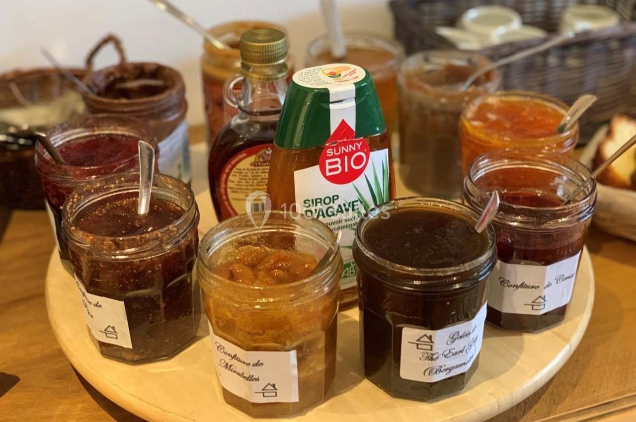 Assortiment de pots de confiture et de sirop d'agave disposés sur un plateau en bois, avec paniers en arrière-plan.