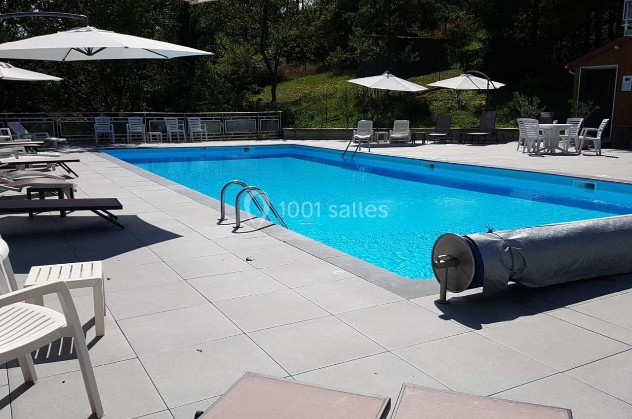 Piscine extérieure avec eau bleue, entourée de chaises longues, parasols et végétation en arrière-plan.