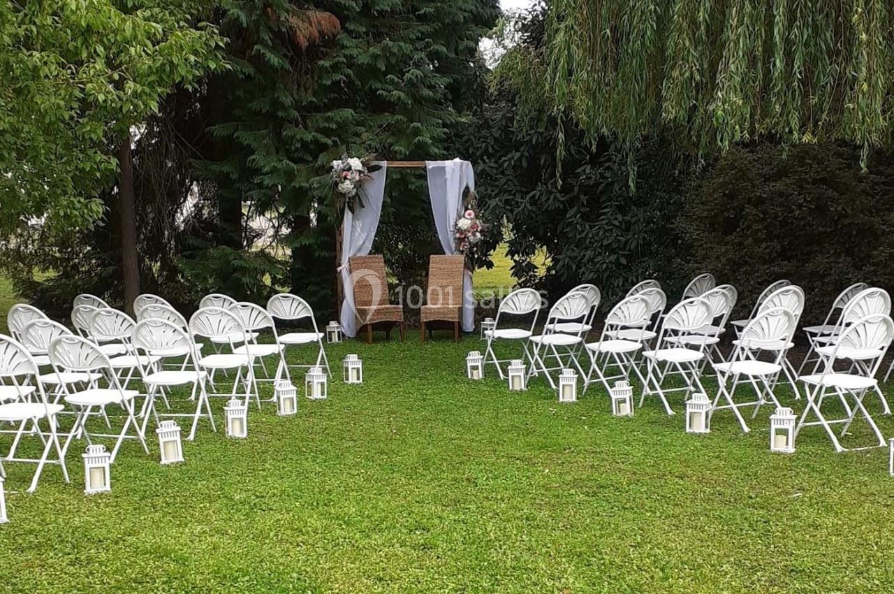 Chaises blanches disposées en allée face à une arche décorée de fleurs dans un jardin verdoyant.