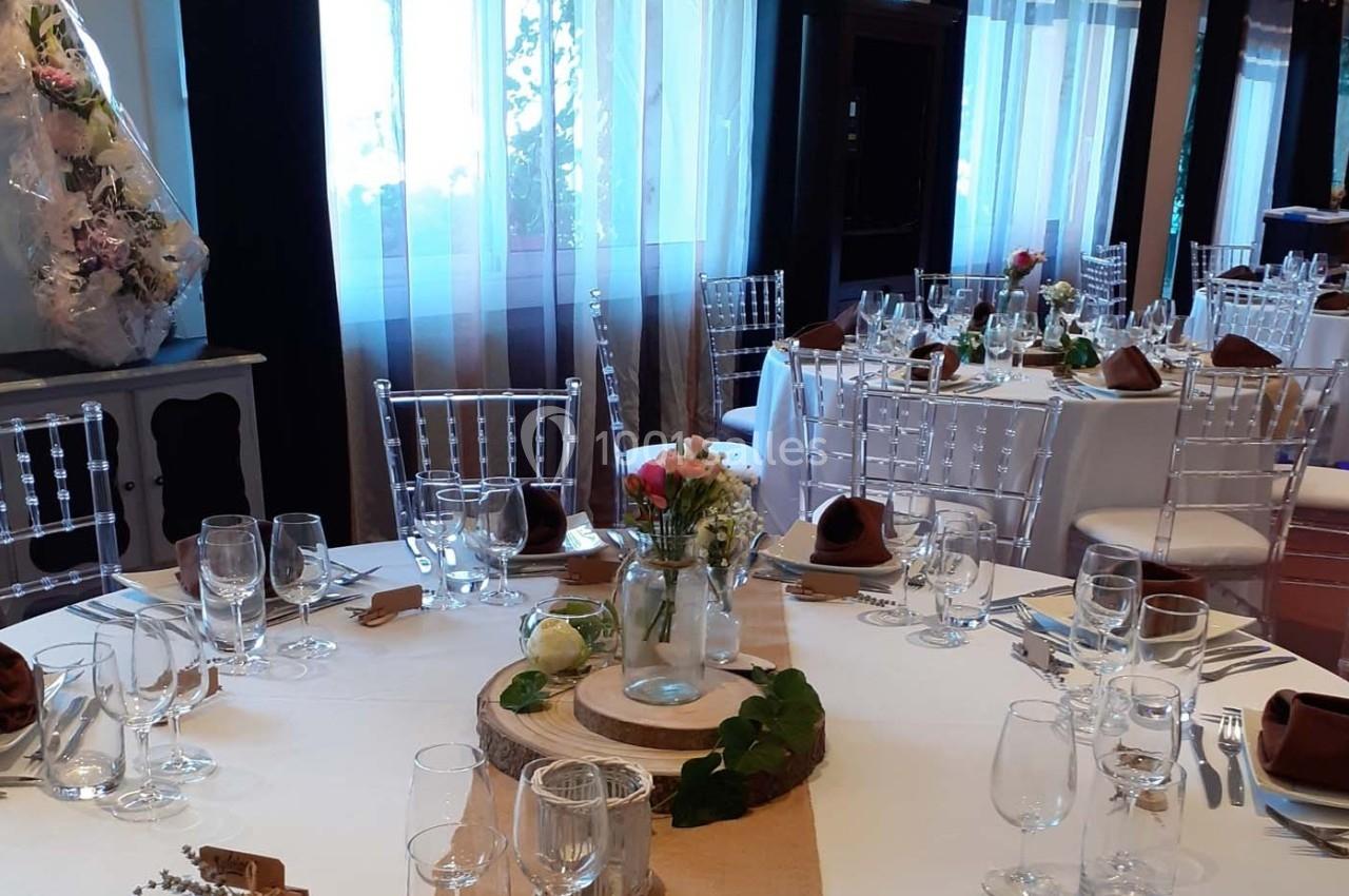 Salle de réception décorée avec des tables rondes dressées, nappes blanches, centres de table floraux et chaises…
