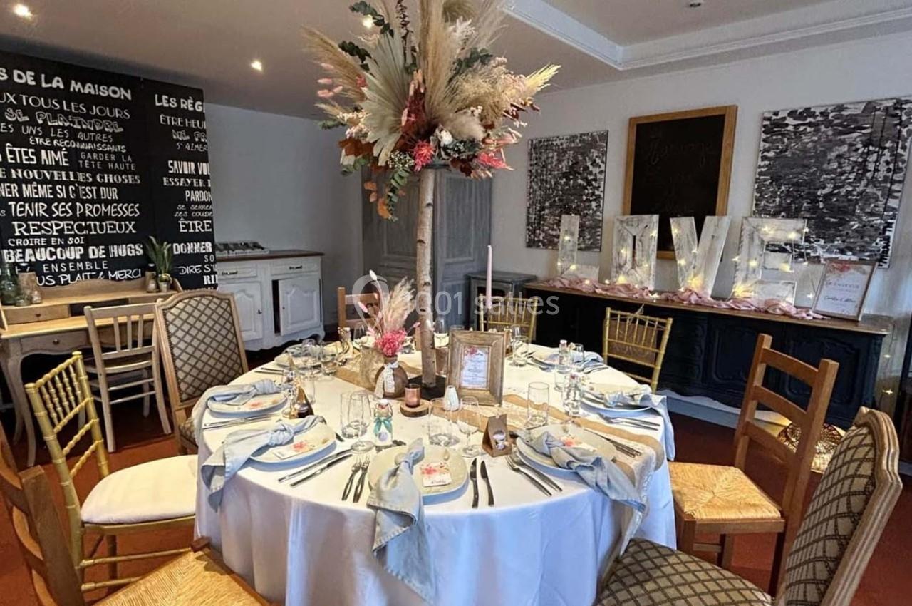 Table ronde décorée pour un événement, avec nappes blanches, serviettes bleues, centre de table floral et lettres lumineuses…