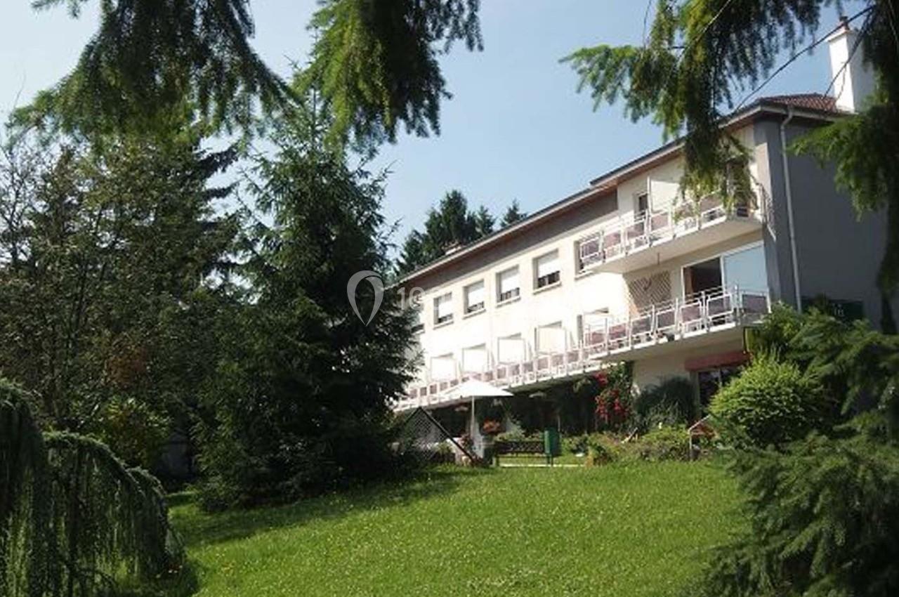 Bâtiment résidentiel entouré d'arbres et d'une pelouse verte, avec balcons et terrasse ombragée.