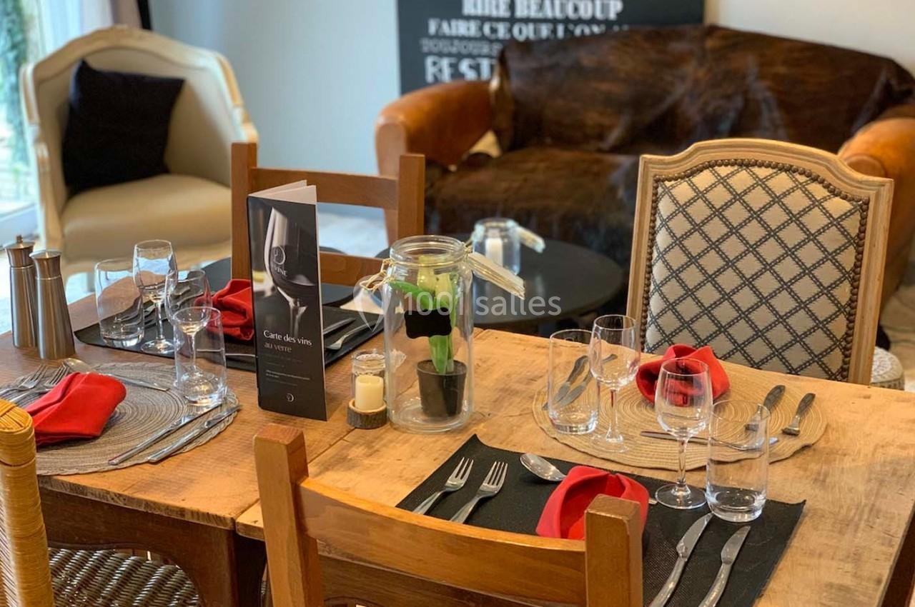 Table dressée avec des verres, des serviettes rouges et un menu, entourée de chaises dans un cadre intérieur chaleureux.